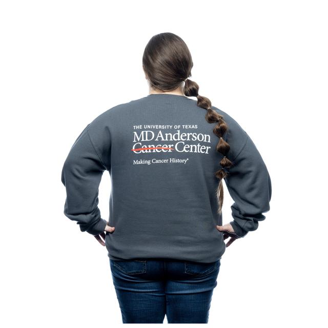 MD Anderson employee wearing a gray crewneck featuring the white cancer strikethrough logo on the chest area and the back featuring the full MD Anderson logo.